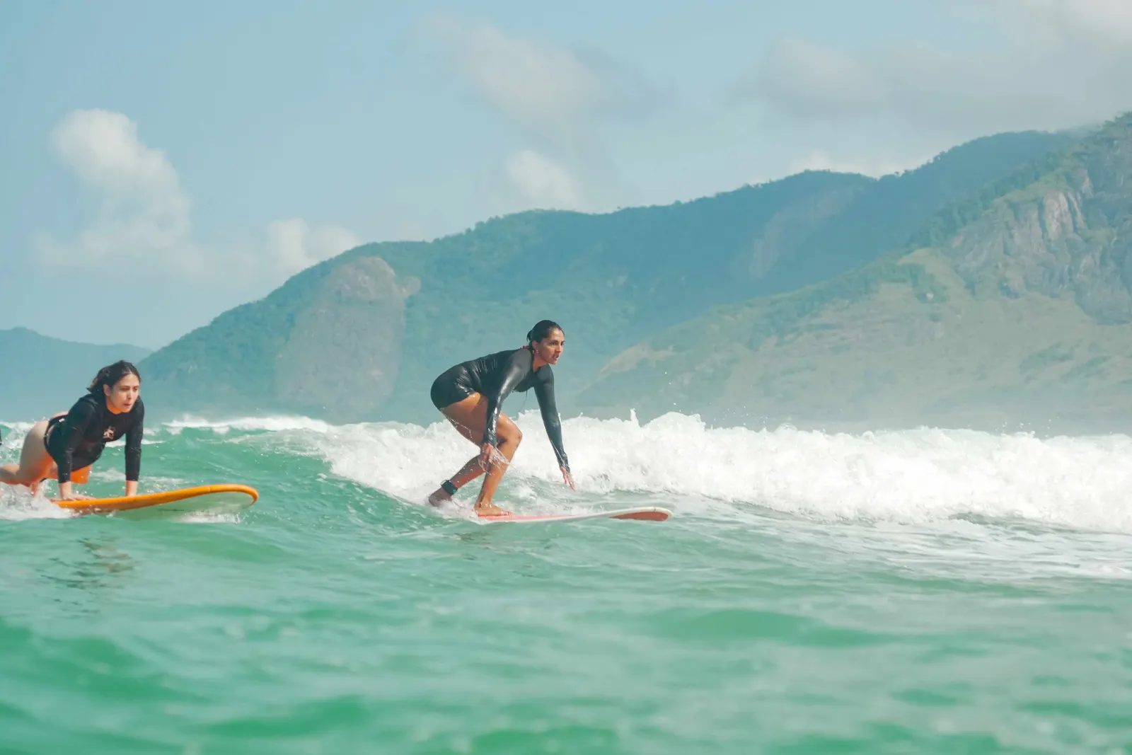 Duas alunas pegando onda na espuma durante a aula de surf