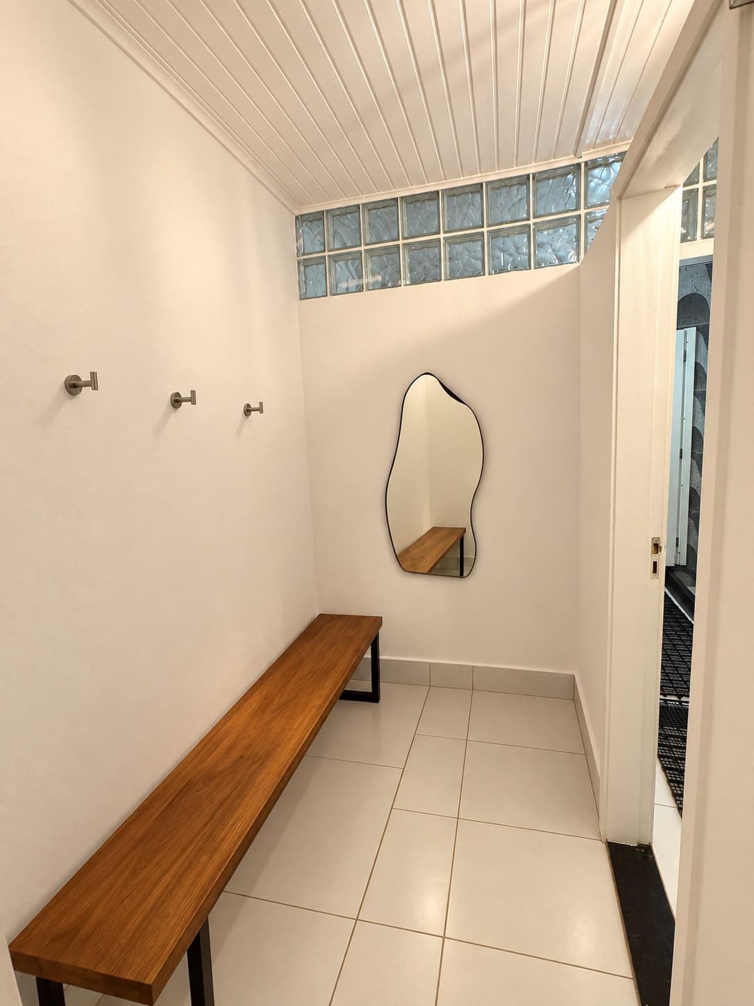 Vestiário com banco de madeira, ganchos e espelho orgânico