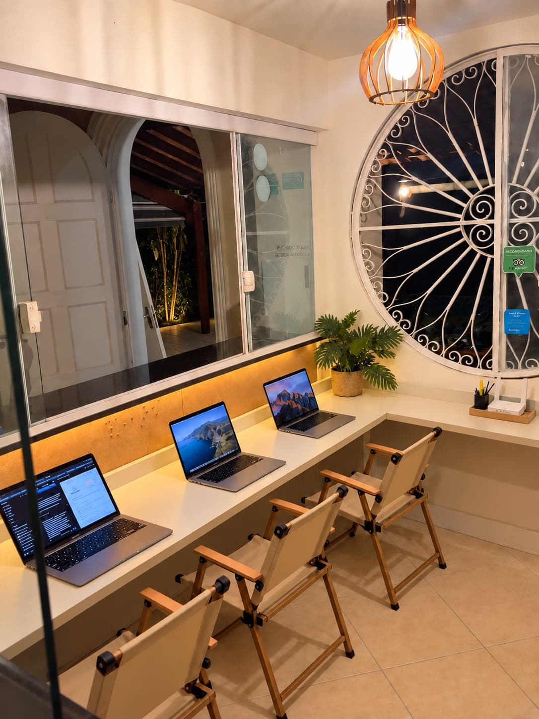 Espaço de coworking com bancada iluminada, notebooks e janela redonda de ferro