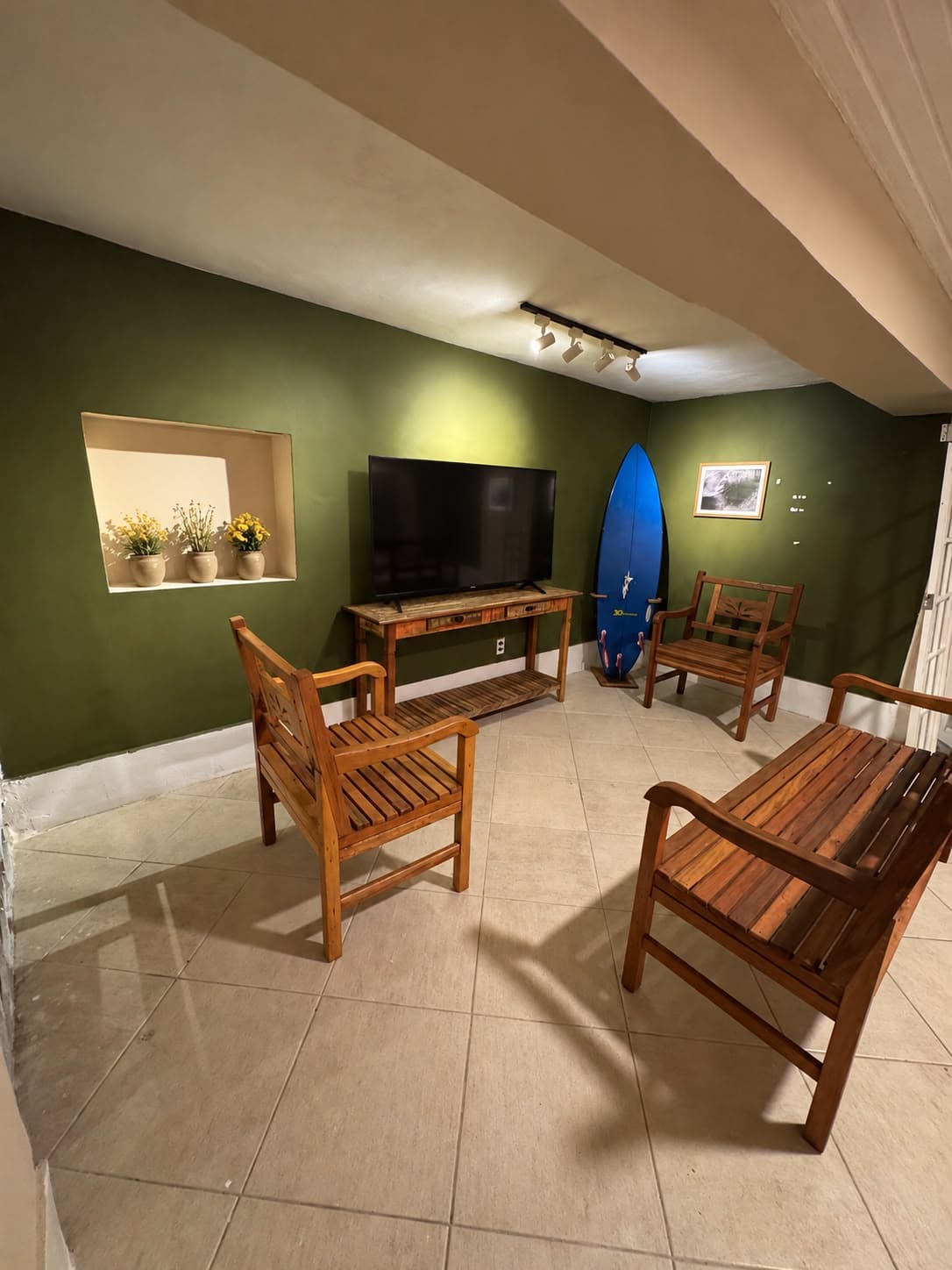 Sala de convivência com parede verde, cadeiras de madeira e prancha de surf azul