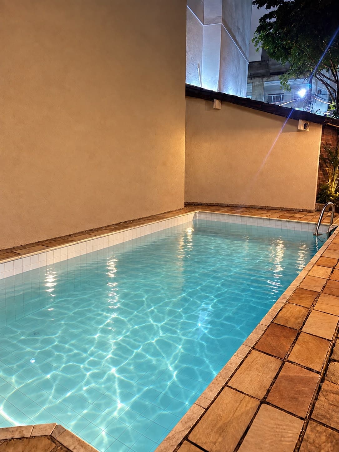 Piscina iluminada à noite com deck de pedra